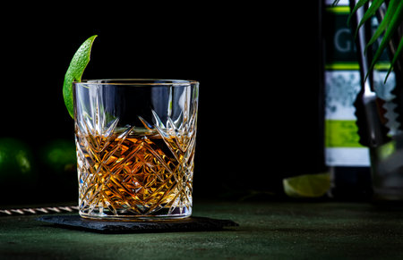 Variation of negroni cocktail with gin, white vermouth and herbal aperitif. Dark green background, steel bar tools