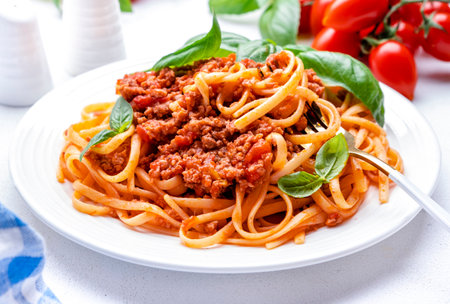 Prepared spaghetti in bolognese sauce or pasta with minced meat and tomatoes decorated green basil, white table background, top viewの写真素材