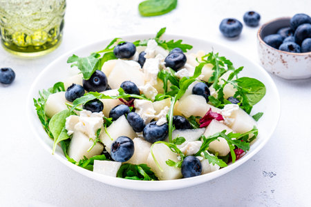 Juicy summer salad with melon, blueberries, ricotta cheese, arugula and spinach., white background, top viewの写真素材