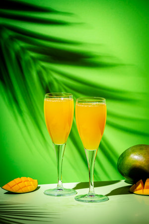 Summer alcoholic cocktail with champagne, mango juice, syrup and ice, green background, hard lightの写真素材