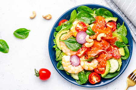 Seafood salad with shrimp, salmon, avocado, spinach, cucumber, tomato, cashew and sesame seeds.. White background, top viewの写真素材