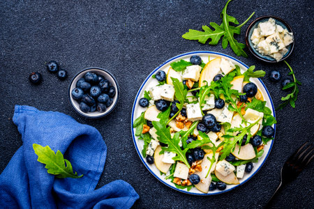 Tasty salad with pears, blueberries, roquefort cheese, arugula and nuts. Black background, top viewの写真素材