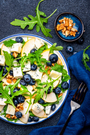 Tasty salad with pears, blueberries, arugula and nuts. Black background, top viewの写真素材