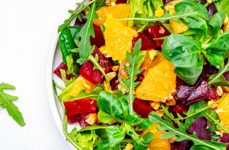 Vegan foodie food beetroot salad with yuicy orange, arugula, lamb lettuce, mini chard and pistachios, white backgroundの写真素材