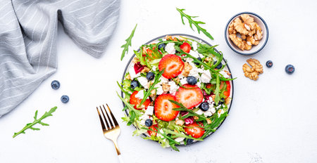 Foodie food salad with strawberry, ricotta cheese, arugula, blueberries and walnuts on white table, top viewの写真素材