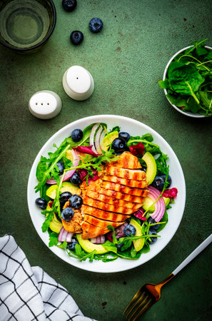 Green salad with grilled chicken, avocado and blueberries, rustic background, top viewの写真素材