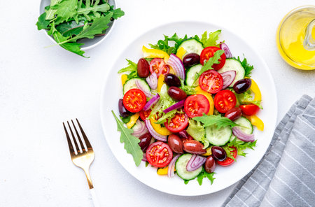 Colorful vegetable salad with olives, tomato, paprika, cucumber, onion, and herbs. White background, top viewの写真素材