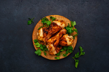 Baked chicken legs orstick drums in spices on wooden serving board, black background, top viewの写真素材