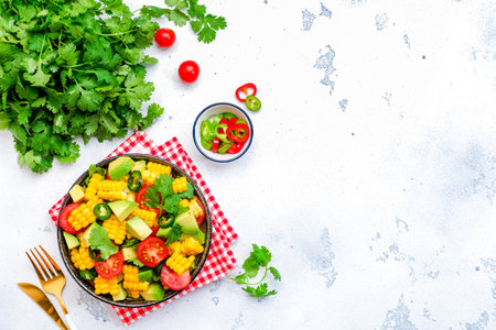Vegan spicy salad with corn, avocado, jalapeno pepper, tomatoes, cilantro, lime and olive oil. White background, top viewの写真素材