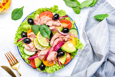 Healthy fat salad with tuna, avocado, olives, vegetables, lettuce and lime. White background, top viewの写真素材