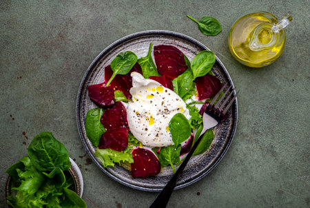 Delicious salad with baked beets, burrata cheese, spinach and olive oil, green background, top view