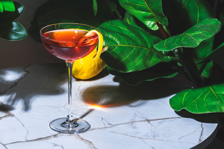 Alcoholic cocktail drink with gin, French aperitif, bitters liqueur and lemon peel. Marble table in lounge bar with green plantsの写真素材