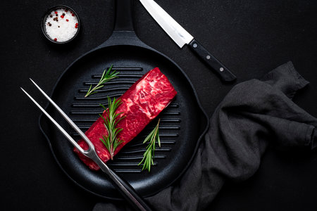 Raw beef sirloin with rosemary on grill pan. Black background, top viewの写真素材