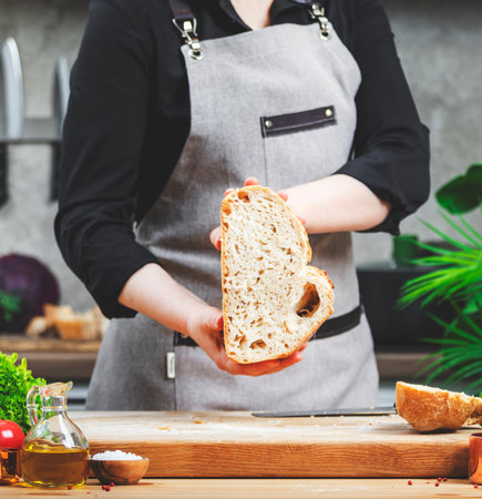 Chef holding sliced â€‹â€‹freshly baked whole grain bread. Cozy kitchen with wooden table,...