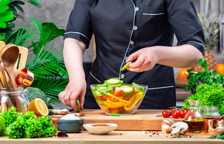 Chef places sliced ââzucchini and paprika into bowl for prepare ratatouille. Cozy kitchen with wooden table, kitchenware, vegetables, herbs and ingredients for cooking. Healthy vegan food, culinary, recipes, food bloggingの写真素材