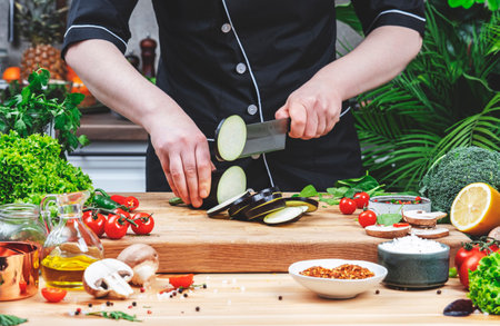 Chef blogger cuts eggplant into wheels. Cozy kitchen with wooden table, kitchenware, vegetables, herbs and ingredients for cooking. Healthy vegan food, culinary, recipes, food bloggingの写真素材
