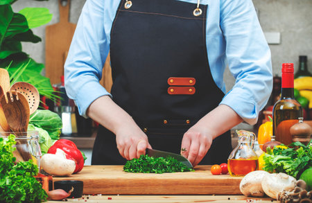 Chef cuts parsley. and dill with santoku knife. Cozy kitchen with wooden table, kitchenware, vegetables, herbs and ingredients for cooking. Healthy vegan eating, culinary, recipes, bloggingの写真素材
