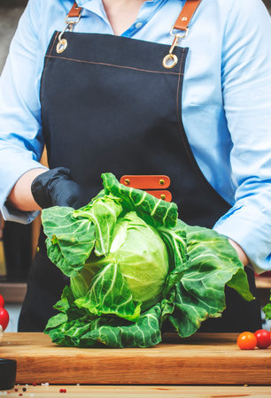 Chef shows organic white cabbage from farm market. Cozy kitchen with wooden table, kitchenware, vegetables, herbs and ingredients for cooking. Healthy vegan eating, culinary, recipes, food bloggingの写真素材