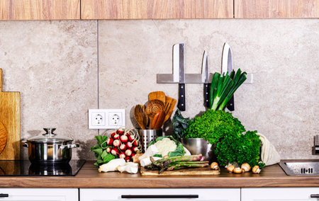 Kitchen countertop with vegetables, herbs and mushrooms for healthy cooking. Food background. Utensils, pans on stove, knives, bowlsの写真素材