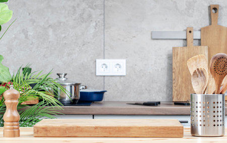 Kitchen table with cutting board, spice grinder and utensils, countertop with pans on induction hob, knivesの写真素材