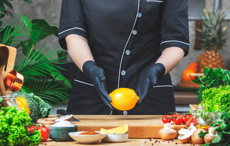 Cooking food in the kitchen. Chef holds lemon in hands. Wooden table, kitchenware, vegetables, herbs and ingredients. Healthy vegan eating, recipes, bloggingの写真素材