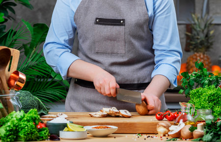 Cooking Food in the Kitchen. Chef cuts mushrooms. Cozy kitchen with wooden table, kitchenware,...