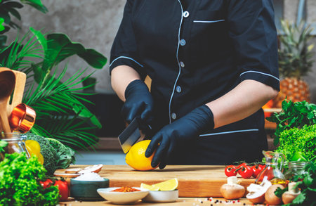 Cooking food in the kitchen. Chef cuts fresh lemon with knife. Wooden table, kitchenware, vegetables, herbs and ingredients. Healthy vegan eating, recipes, bloggingの写真素材