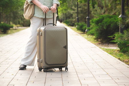 50s year woman with suitcase and bag stay on green summer alley, vacation, travel, outdoor sceneの写真素材
