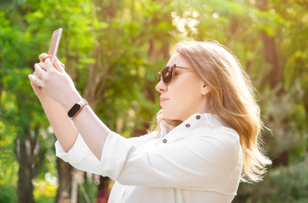 happy, carefree, smiling blonde woman in sunglasses chatting on cell phone via video link or takes a...