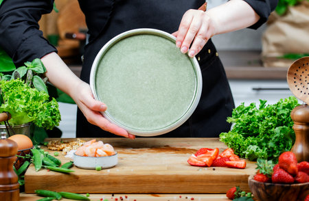 Cooking food in the kitchen, chef holds clean plate, fresh vegetables and fruits on wooden board Preparing colorful vegan dish, healthy cooking, eating, bloggingの写真素材