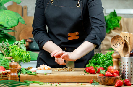 Chef cooking food in the kitchen. Cook cuts walnuts, prepare gourmet salad. Wooden table, kitchenware, vegetables, herbs and ingredients. Healthy vegan eating, recipes, bloggingの写真素材
