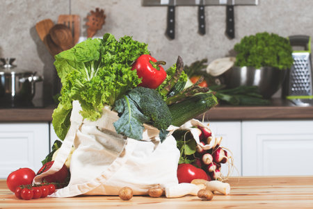 Colorful vegetables and fresh herbs from a farmers market are arranged in an eco-friendly bag on a well-designed kitchen table.の写真素材
