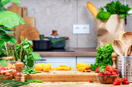 Food background. Healthy eating, cooking and blogging scene. Cutting board with apricots, strawberry, peas, lettuce and other on cozy kitchen with wooden table, kitchenware and utensilsの写真素材