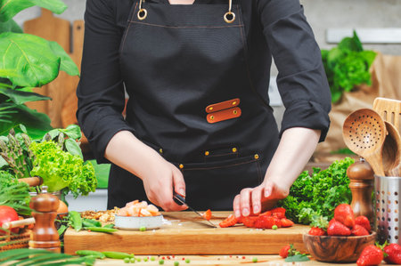 chef skillfully chops vegetables on a wooden cutting board in a lively kitchen adorned with fresh produce and plants, promoting healthy eating.の写真素材
