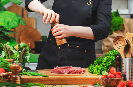 chef sprinkle beef steak with pepper from the mills prepare a healthy dish in a cozy kitchen, using fresh farm herbs and vegetablesの写真素材