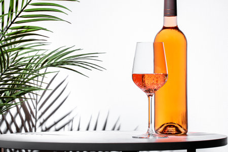glass of rose pink wine next to a bottle on a stylish table with palm leaves in the background during a lively celebrationの写真素材