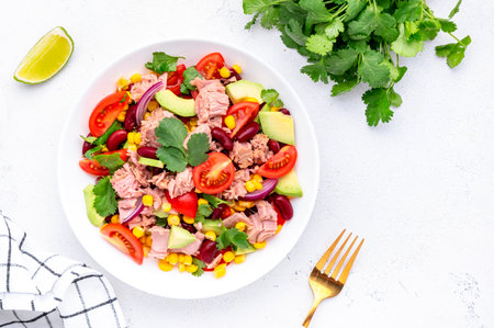 Mexican style salad with canned tuna, avocado, corn, red beans, cherry tomatoes and cilantro, white table background, top viewの写真素材