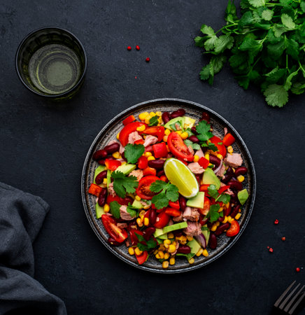 Tex-mex salad with canned tuna, avocado, corn, red beans, cherry tomatoes, cilantro and lime dressing, black table background, top viewの写真素材