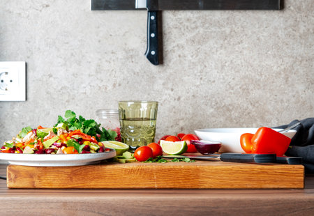 Preparing yummy salad with tuna, corn, avocado, beans, tomatoes and cilantro in plate on kitchen countertop and ingredients for preparation on wooden cutting boardの写真素材