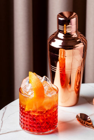 vibrant negroni sbagliato cocktail on a table beside a cocktail shaker, garnished with orange peel and ice.の写真素材