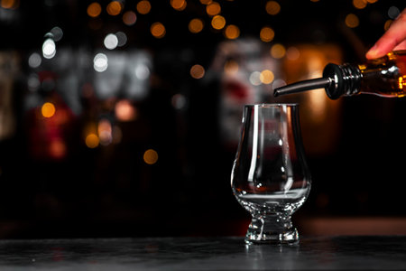 hand carefully pours whiskey into a glass, creating an inviting atmosphere in a stylish bar with soft lighting elements.の写真素材
