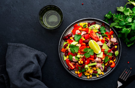 Tex-mex salad with canned tuna, avocado, corn, red beans, cherry tomatoes, cilantro and lime dressing, black table background, top viewの写真素材