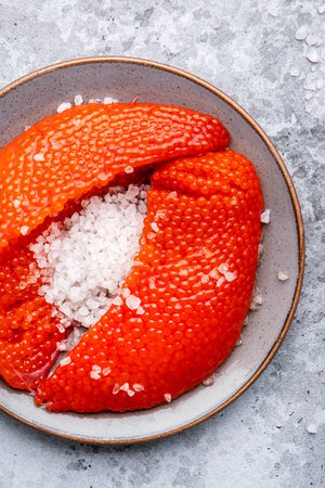 Fresh whole raw red caviar extracted from live trout or salmon with sea salt, gray background, top...