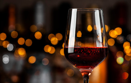 A glass filled with rich red wine sits elegantly, surrounded by soft golden lights in a warm and...