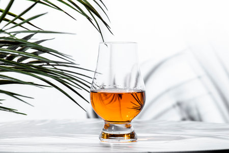 Single malt scotch whiskey in a glencairn glass surrounded by lush foliage, highlighting the golden...