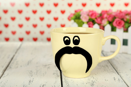 Yellow cup with paper mustache on white wooden backgroundの写真素材