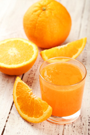 Orange fruit and glass of juice on white wooden backgroundの写真素材