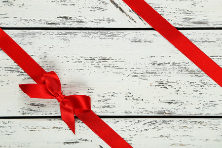 Red ribbon with bow on white wooden backgroundの写真素材