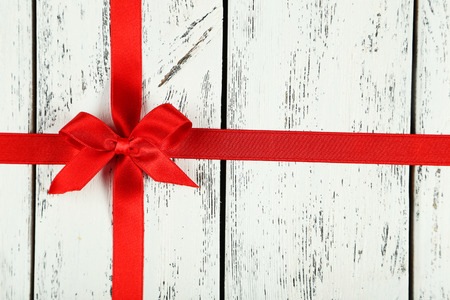 Red ribbon with bow on white wooden backgroundの写真素材