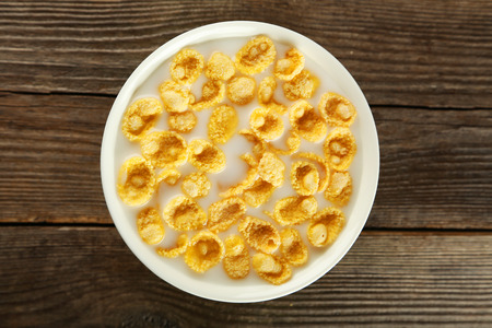 Bowl of cornflakes with milk on brown wooden backgroundの写真素材